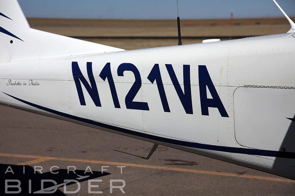 A close-up view of the N121VA registration number on the white fuselage with blue stripes of the Tecnam P2010.
