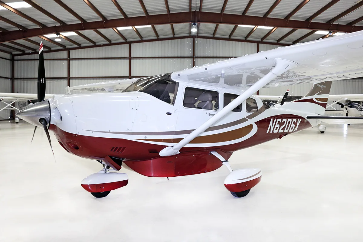 A front-left view of a white and red Cessna Stationair TC N6206X parked inside a hangar.