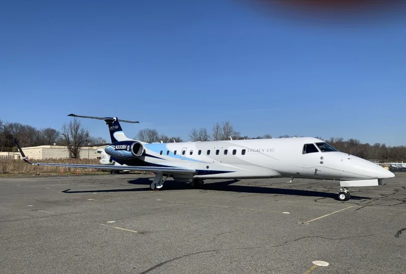 A white and blue Embraer Legacy 650 business jet with registration N333BH parked on an asphalt tarmac under a clear blue sky.