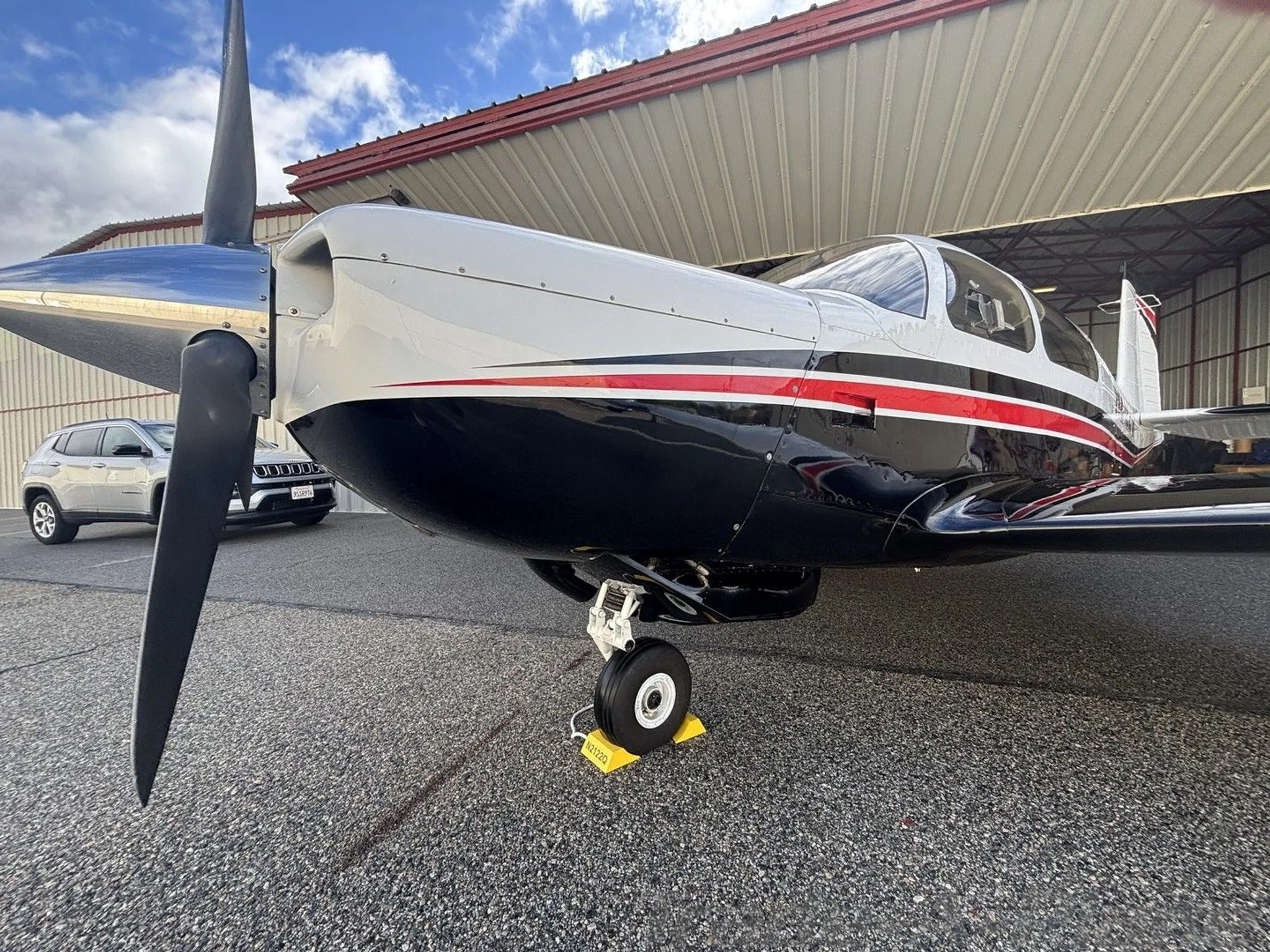 A close-up front view of the propeller and nose of a white and black Mooney M20K aircraft, registration N2122Q, parked in a hangar.