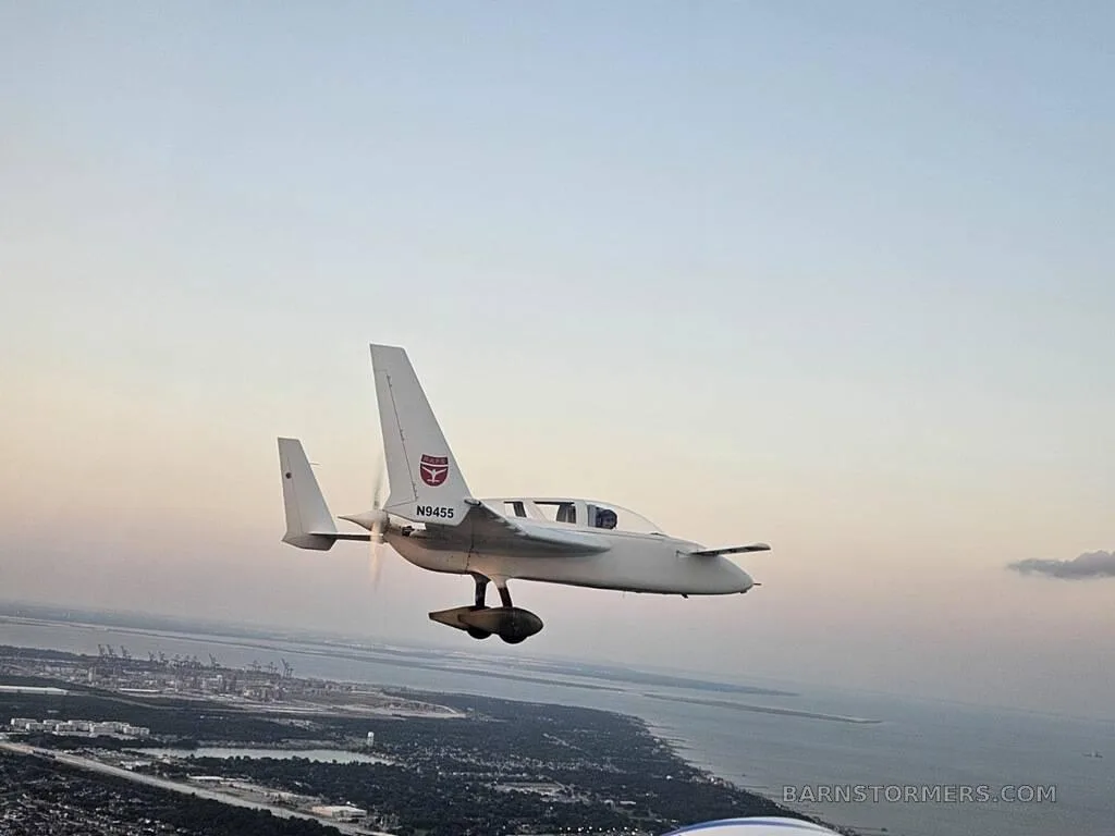 A white Rutan Long-EZ aircraft with registration N9455 flying over a coastal area at sunset.