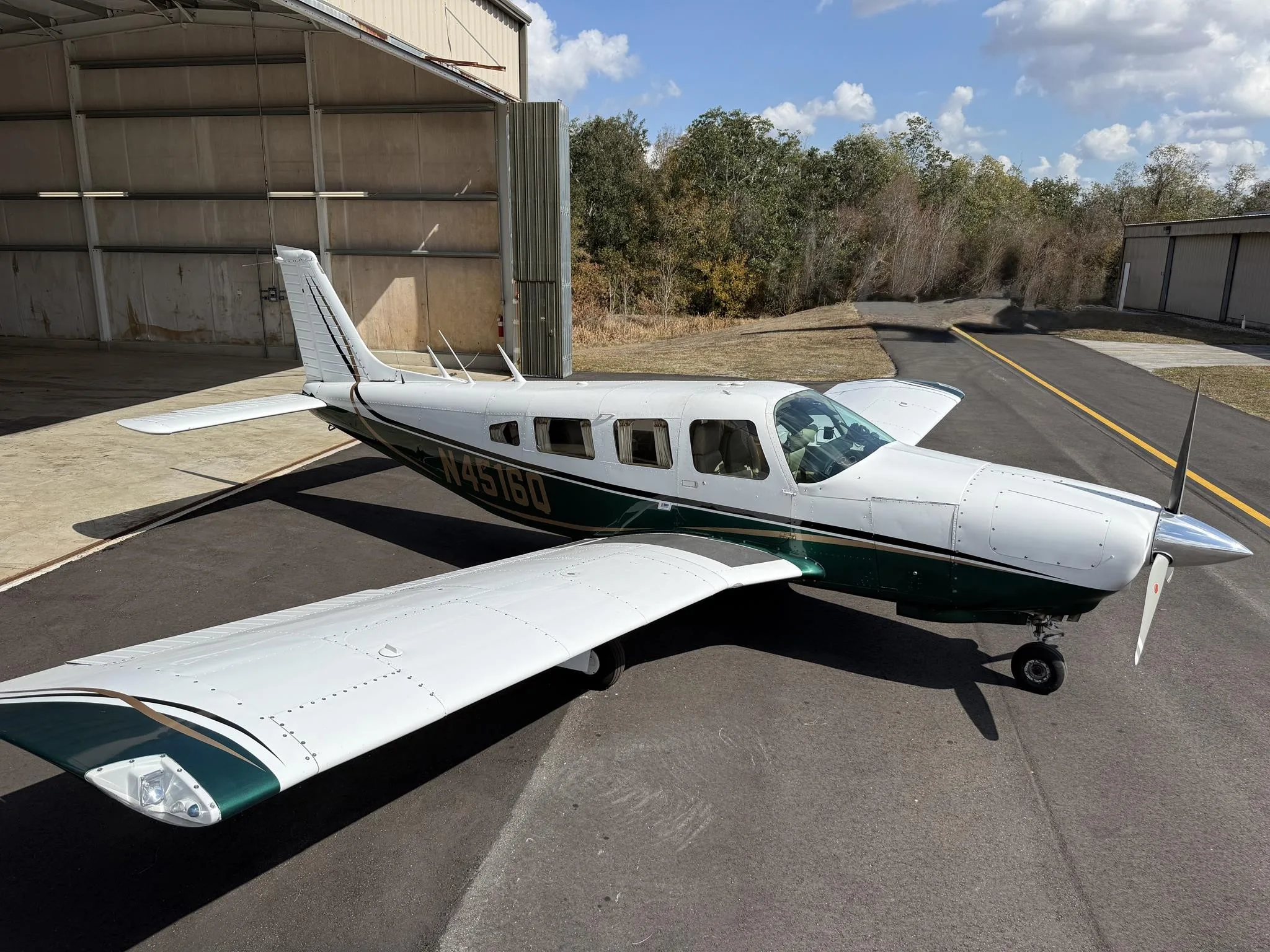 A white and green Piper PA-32R-300 Cherokee Lance II (N4516Q) parked on an asphalt ramp outside a hangar.