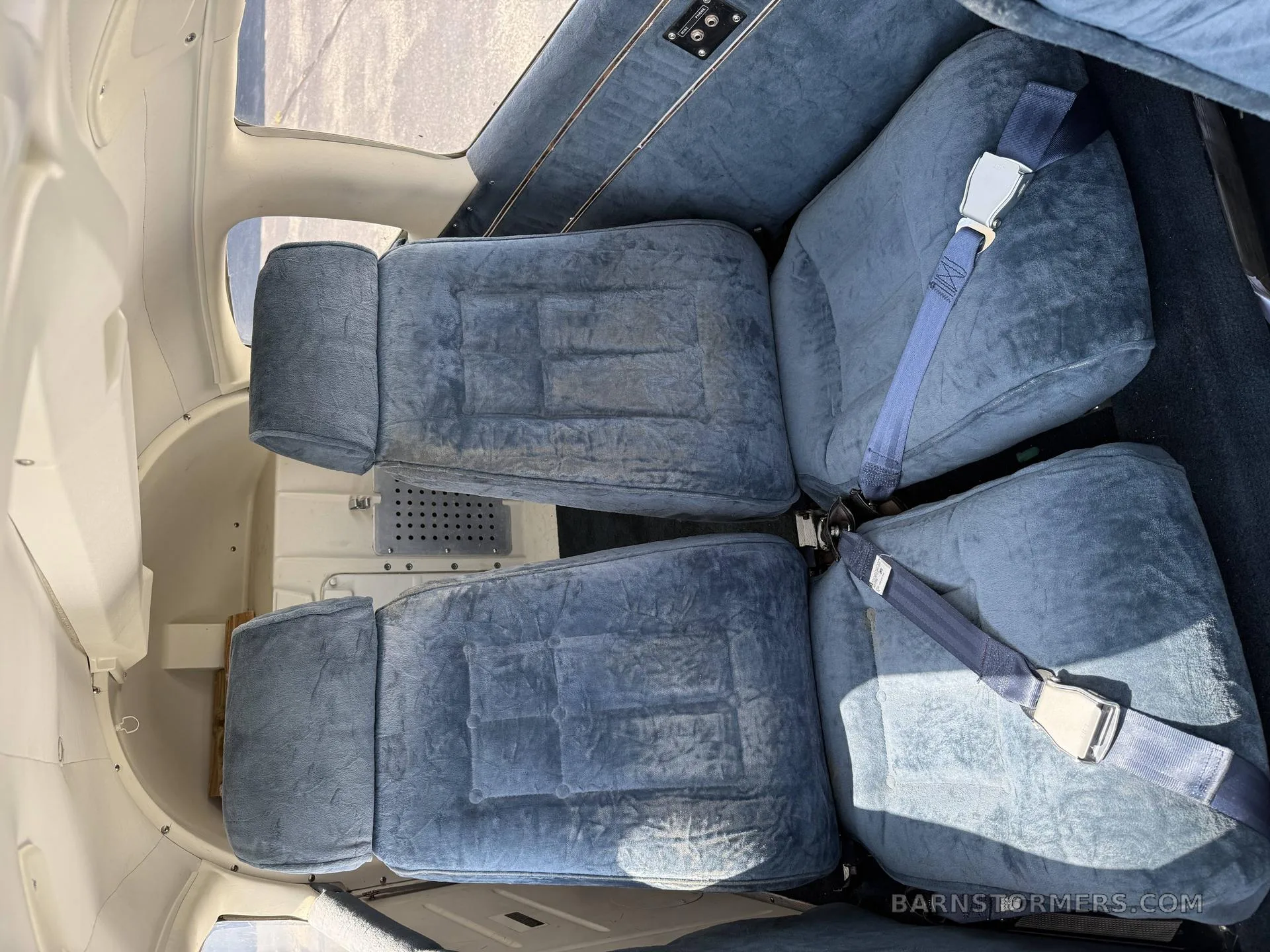 The rear cabin of a Piper aircraft with two rows of blue fabric seats and seatbelts.