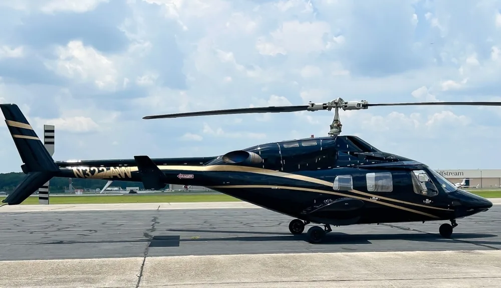 Side view of a black Bell 430 helicopter with gold stripes, registration N322AW, on an airfield.