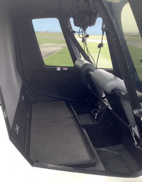 The black floor and side panel of a helicopter interior, with a view of an airfield through the window.