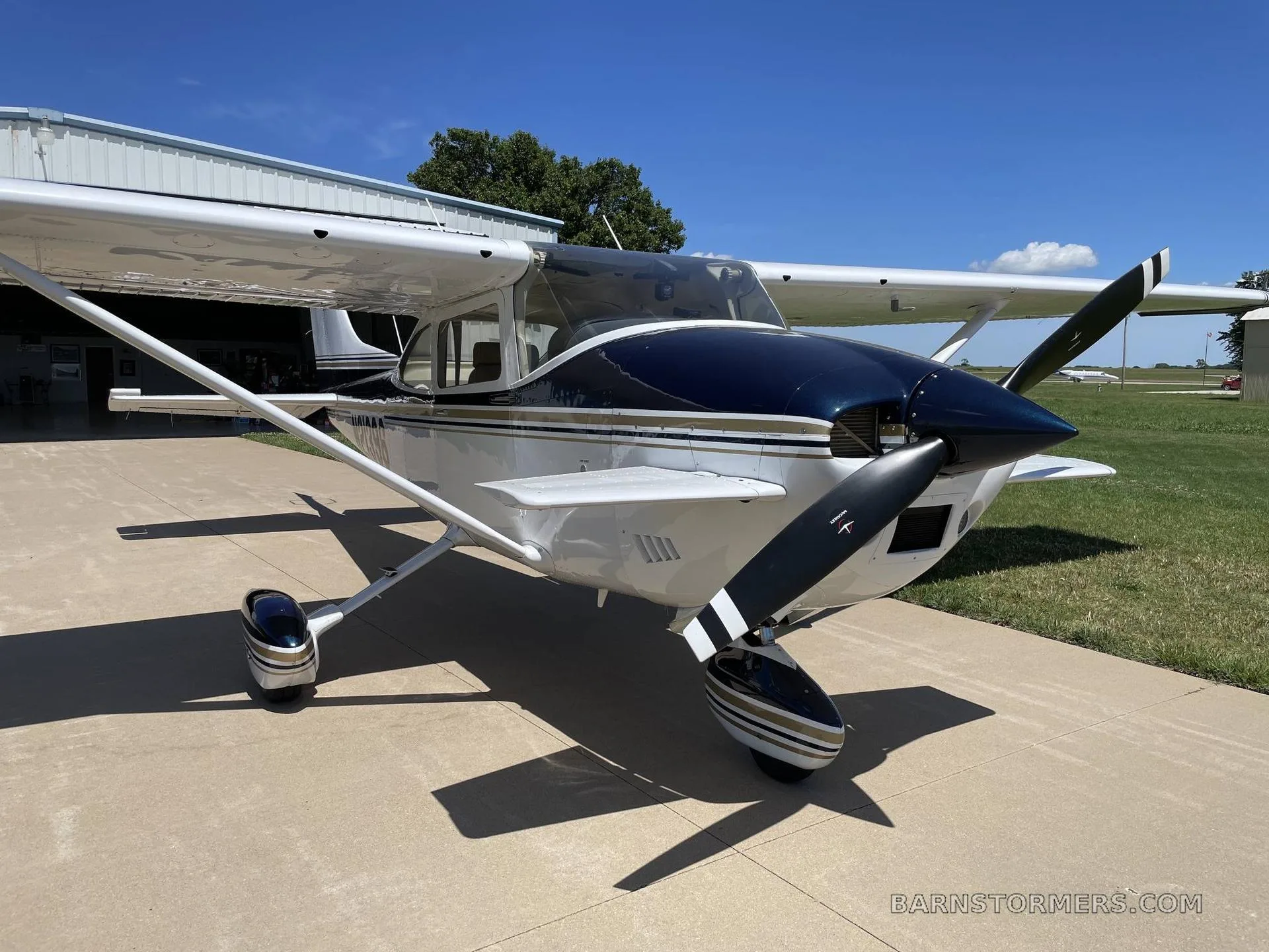 A white and dark blue Cessna 172 with a propeller, parked on a tarmac in front of a hangar.