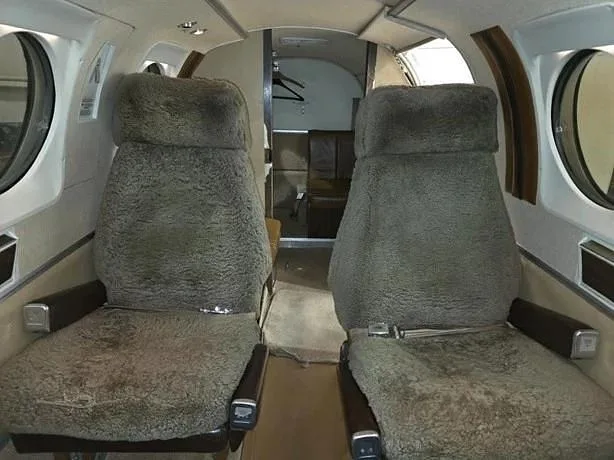 Two sheepskin-covered passenger seats are visible in the aircraft cabin, looking towards the rear.