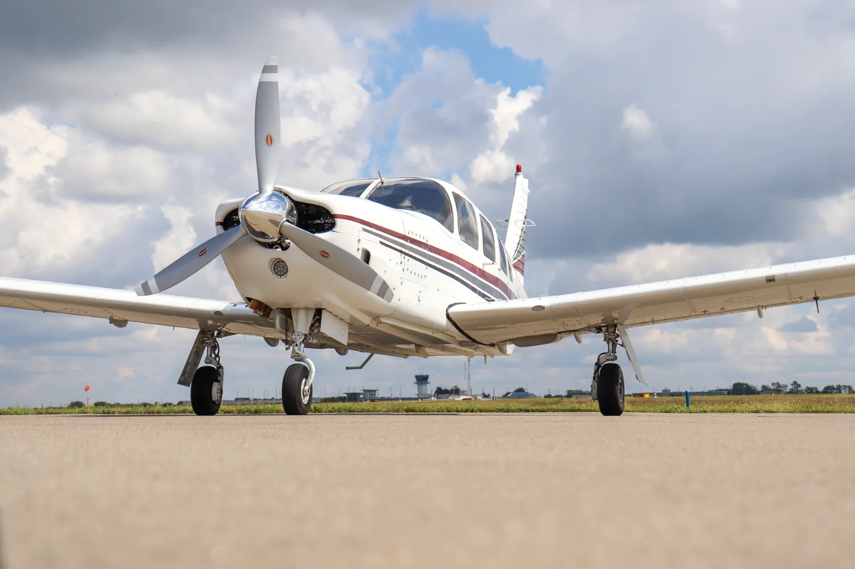 A white Piper Lance (N24MT) with red and grey stripes is parked on an airfield, viewed from a very low front angle.