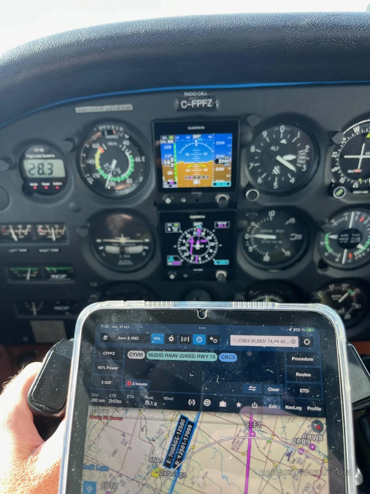 A close-up view of an aircraft's instrument panel, featuring a mix of traditional gauges and digital screens, with a pilot's hand holding a tablet displaying a navigation app.