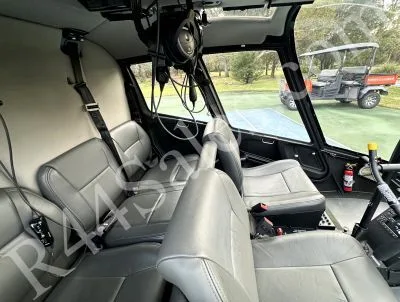 The grey leather interior of a helicopter cabin with four seats and a fire extinguisher visible.