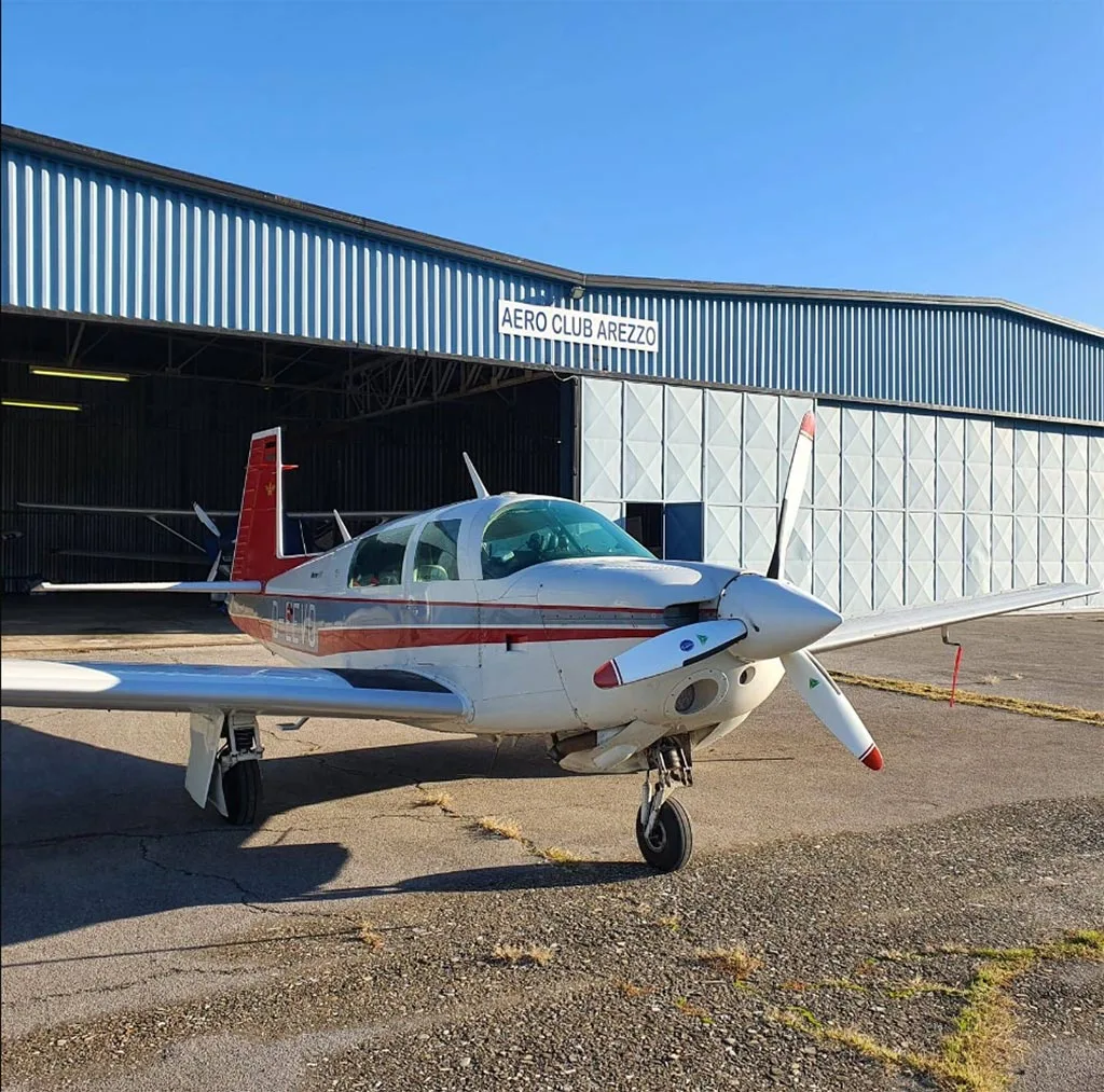 A white and red Mooney M20J aircraft (D-EEVO) parked on an tarmac in front of an "AERO CLUB AREZZO" hangar.