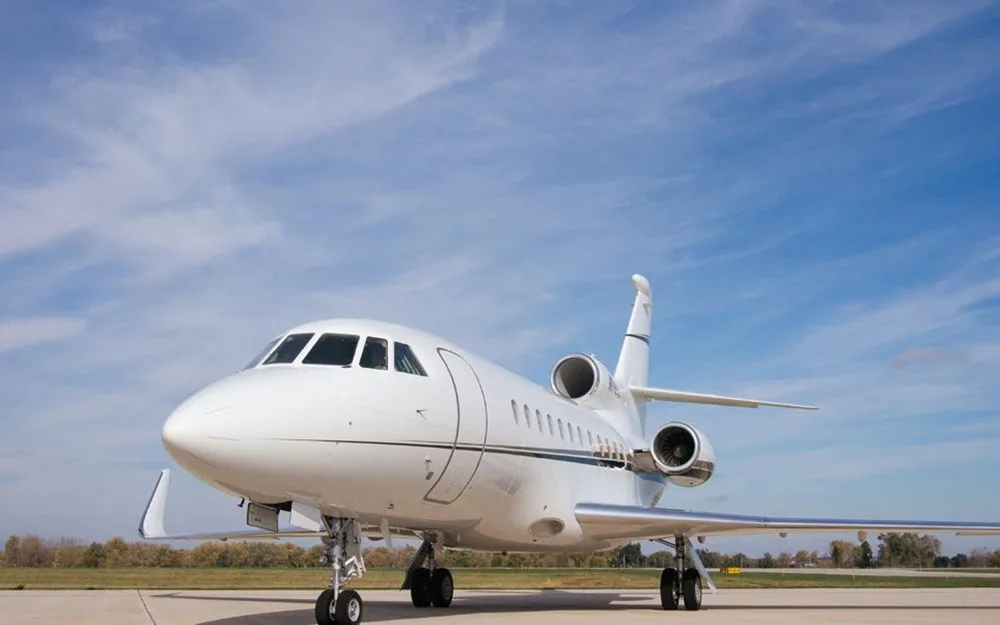 A front-quarter view of a white Dassault Falcon 900EX business jet with black and grey stripes, parked on an airfield.