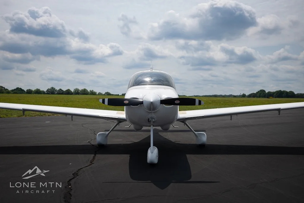 A front view of the white Cirrus SR20 aircraft N622DA parked on an asphalt runway under a cloudy sky.