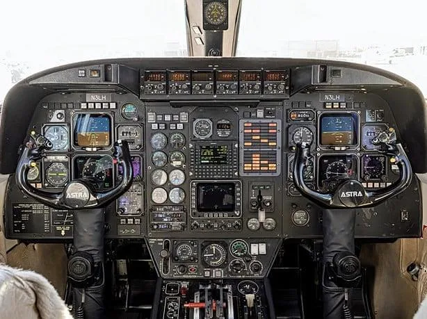 The cockpit of an Astra business jet, featuring a complex instrument panel with multiple screens and two control yokes.