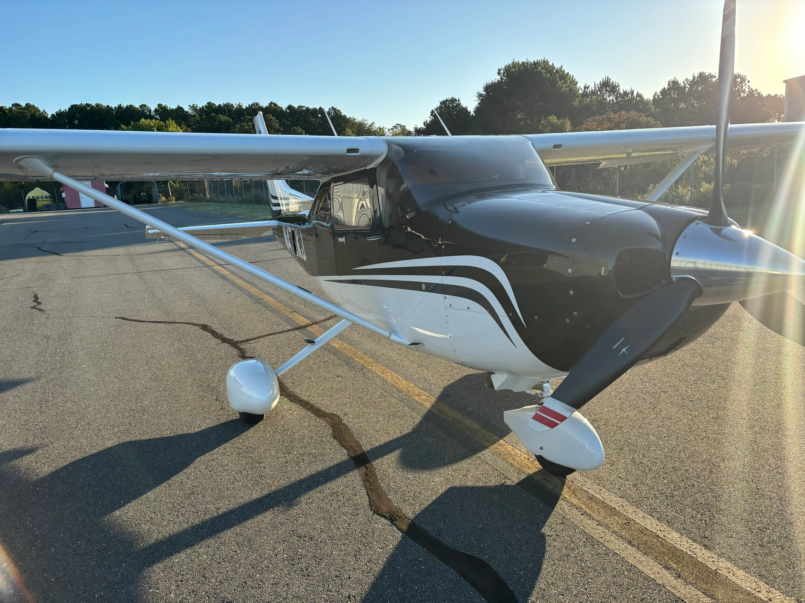 A black and white single-engine propeller aircraft on an tarmac at sunset.