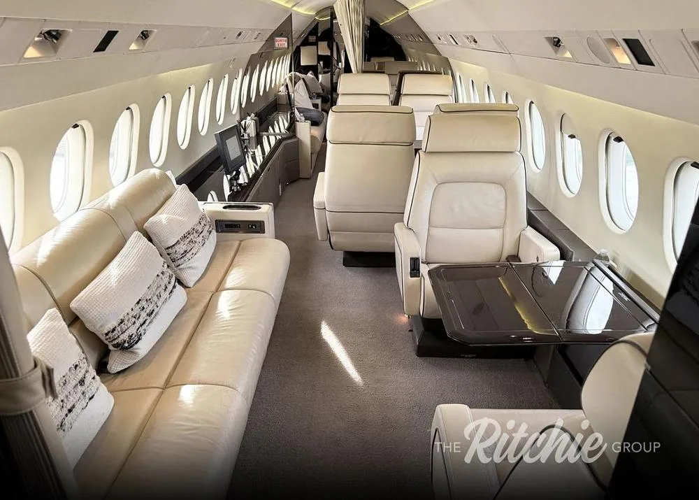 The luxurious interior cabin of the business jet, featuring a beige leather sofa and individual seats.