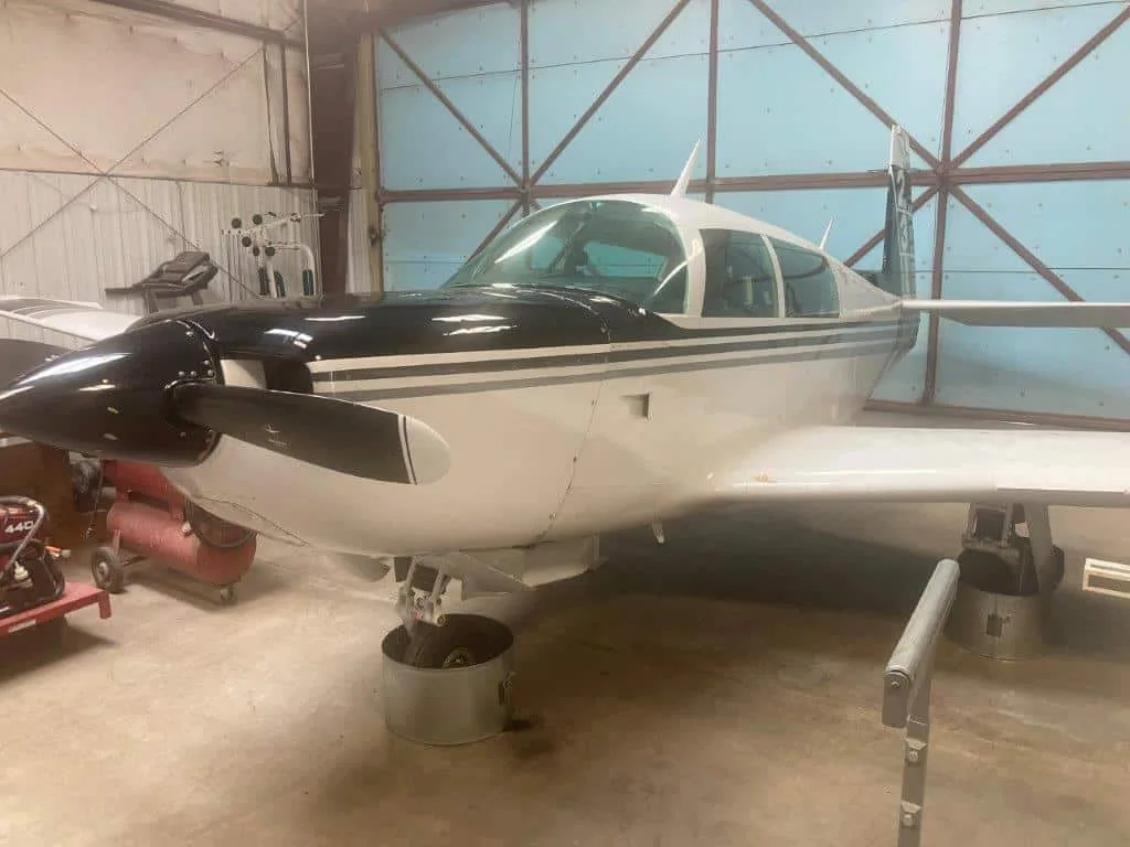A white and black Grumman American AA-5 Traveler aircraft, N1047A, on stands inside a hangar.