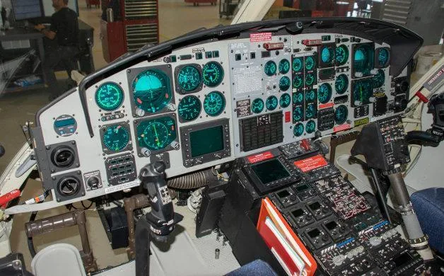 The cockpit of a helicopter features numerous green-lit gauges, screens, and control panels.