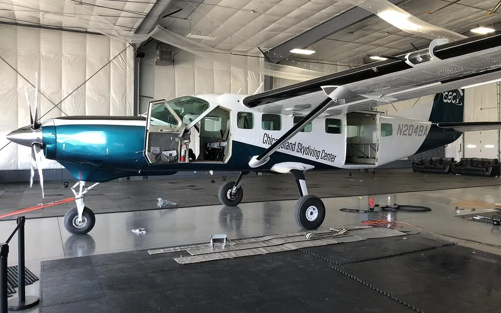 A teal and white single-engine turboprop aircraft with open doors sits in a hangar.