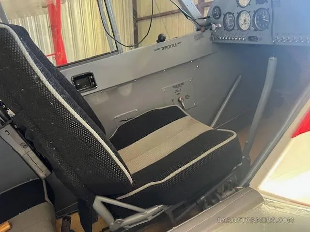 A black and tan fabric pilot's seat inside the aircraft cabin, with part of the instrument panel visible.