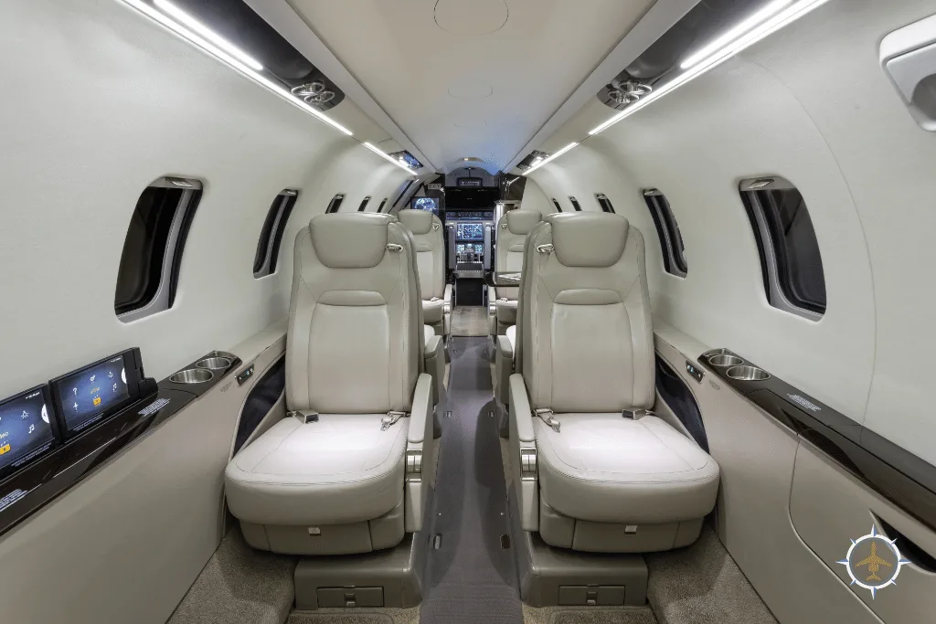 A luxurious aircraft cabin with light-colored leather seats and screens on the side panels, looking towards the cockpit.