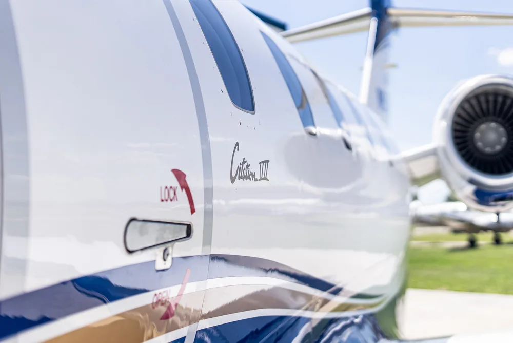 A close-up of the white and blue Cessna Citation III fuselage, showing the 'Citation III' text and a door handle.