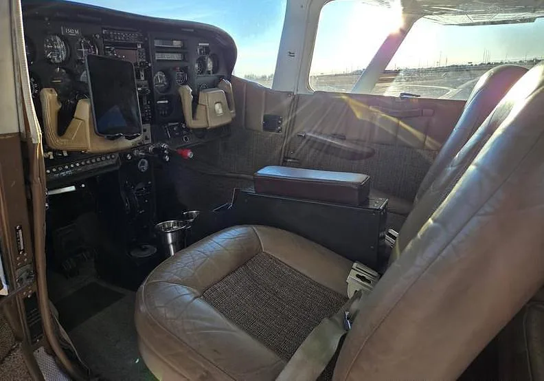 The cockpit and front cabin of a Cessna aircraft with brown leather seats and instrument panel visible.