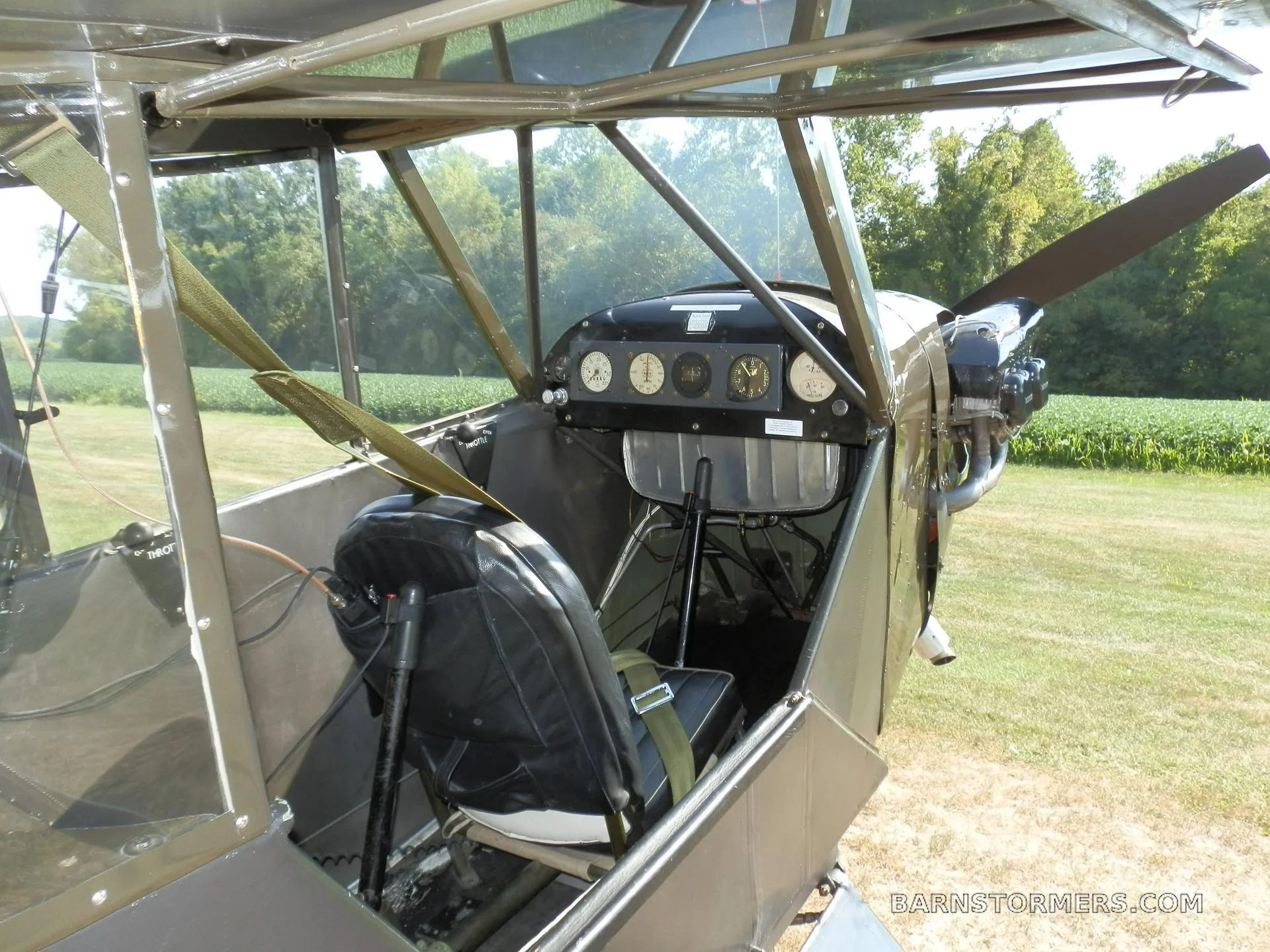 An open cockpit view of a small aircraft, showing the pilot's seat, instrument panel, and engine cowling.