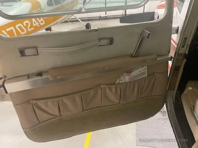 The tan interior door panel of an aircraft, showing storage pockets and a window.