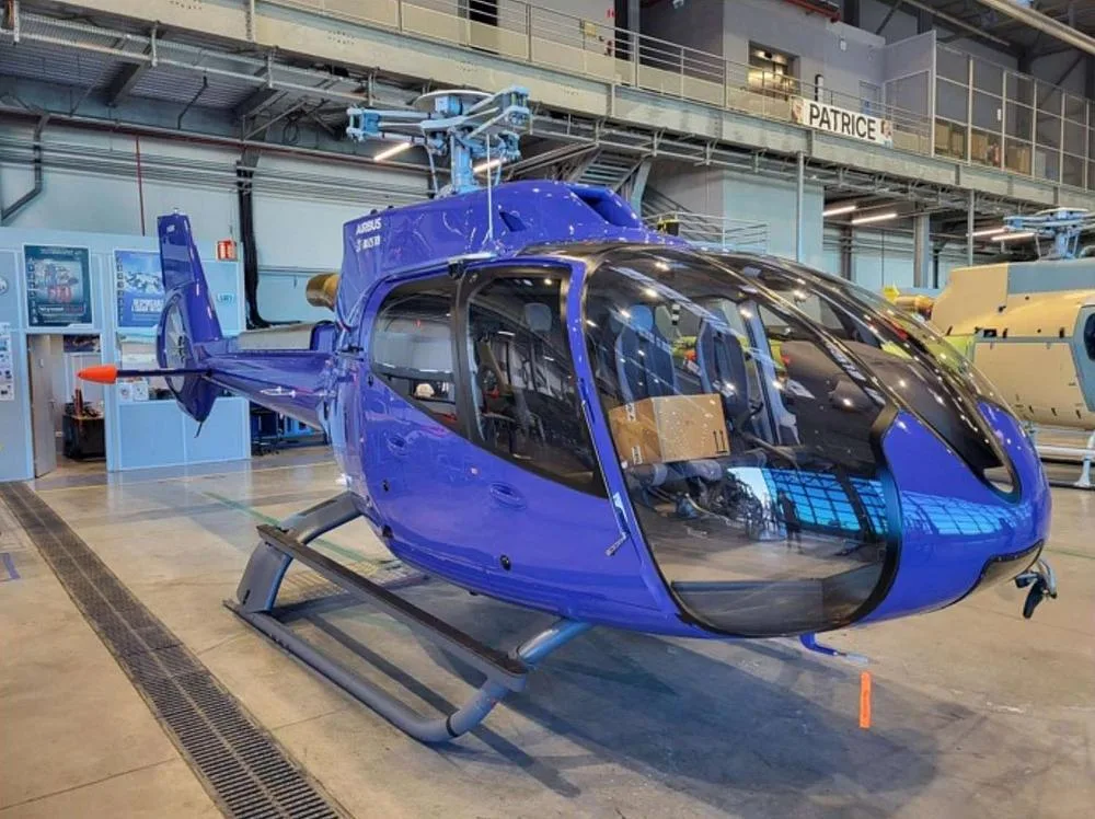 A blue Airbus H135 helicopter with skids, seen from the front-right in a hangar.
