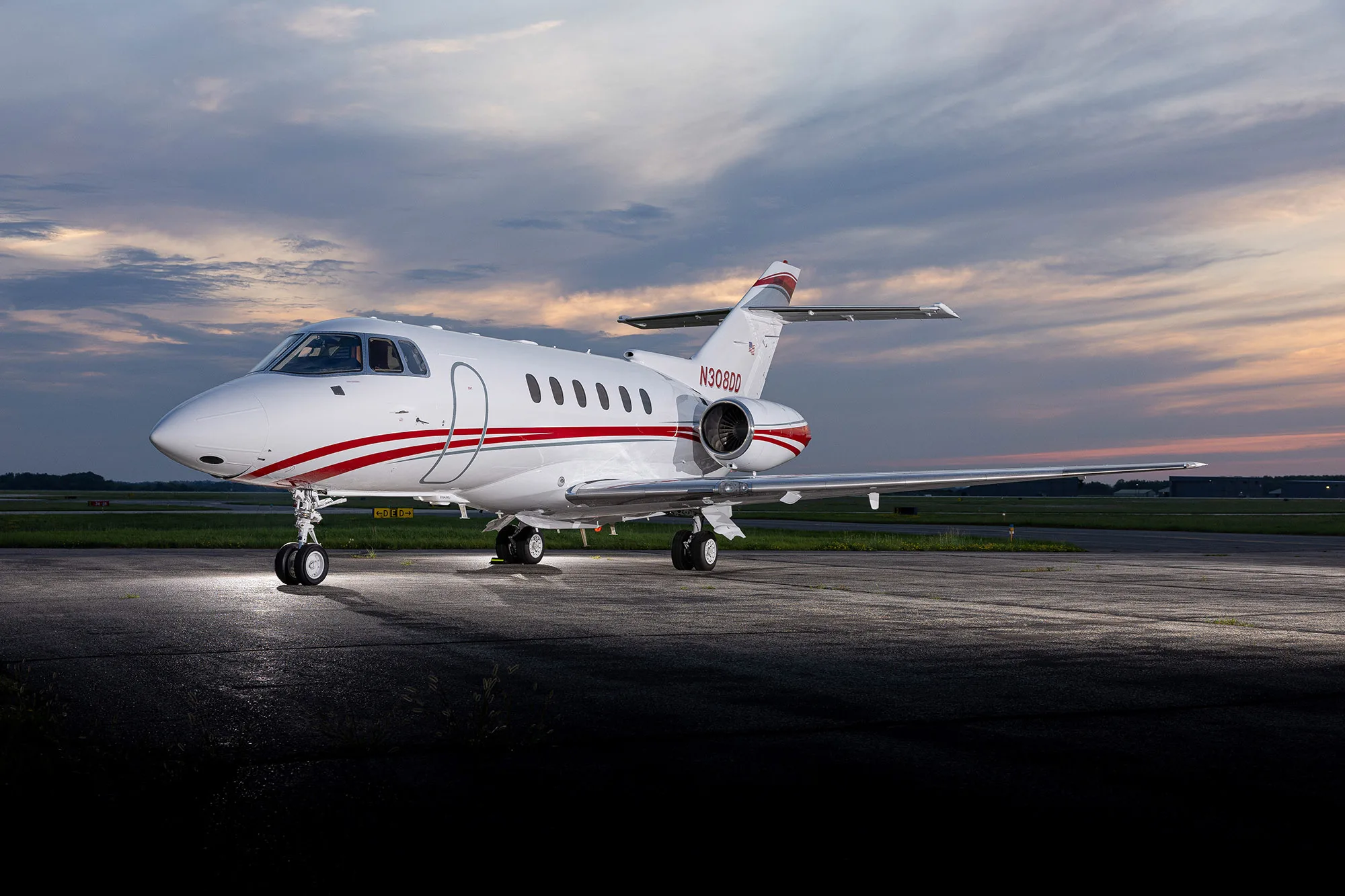 A white business jet with red stripes, registration N308DD, parked on an airfield at dusk, viewed from the front.