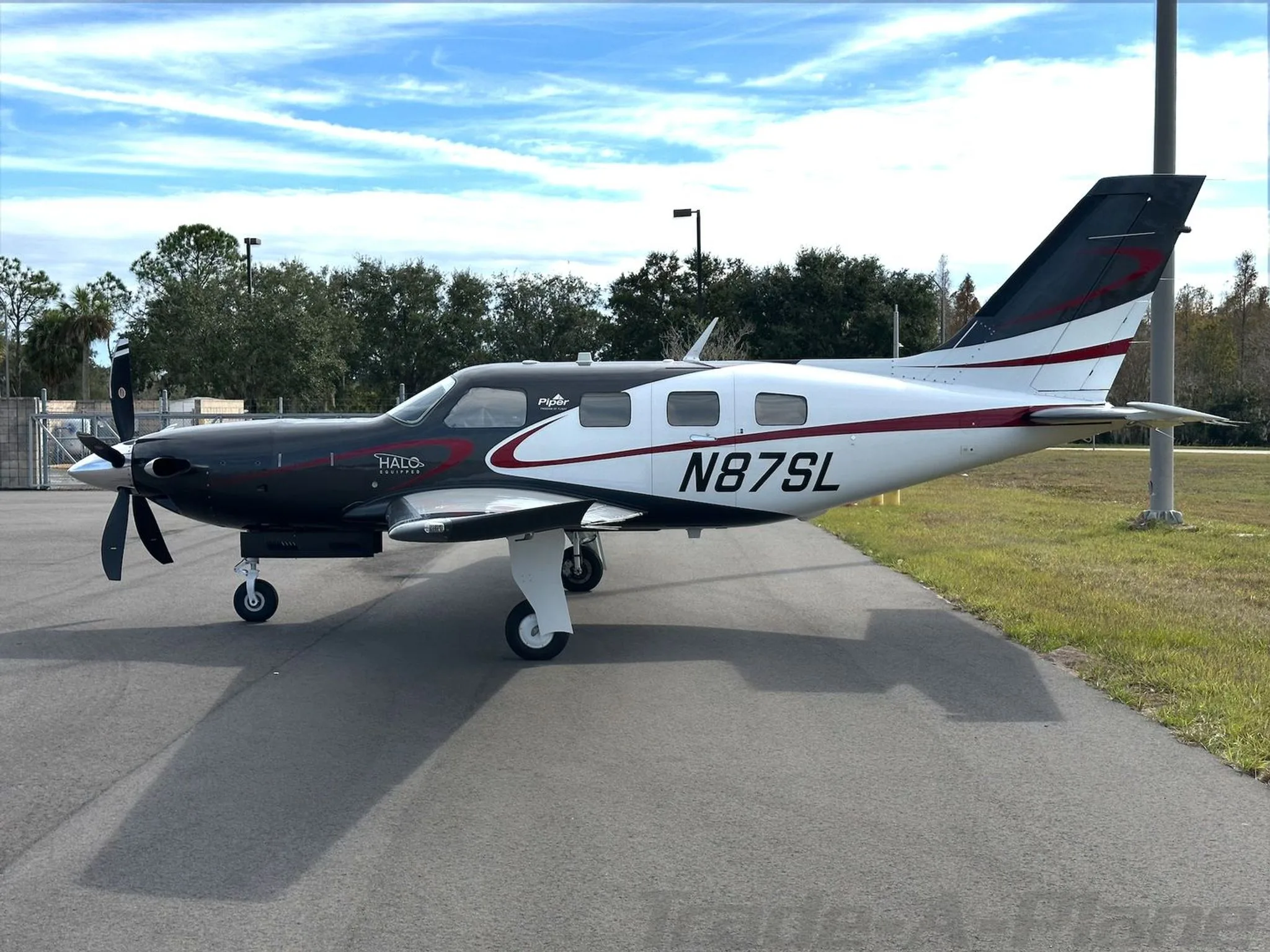 A side view of the Piper M600/SLS aircraft N87SL, highlighting its black and white paint scheme with red stripes, parked on an airfield.