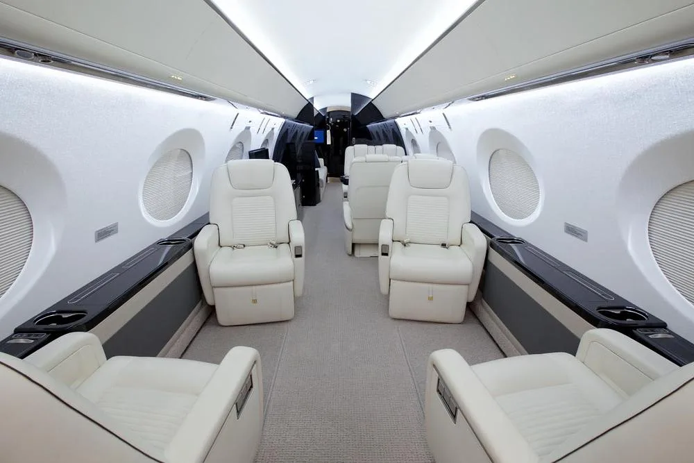 The luxurious interior cabin of a business jet with cream leather seats and dark accents.