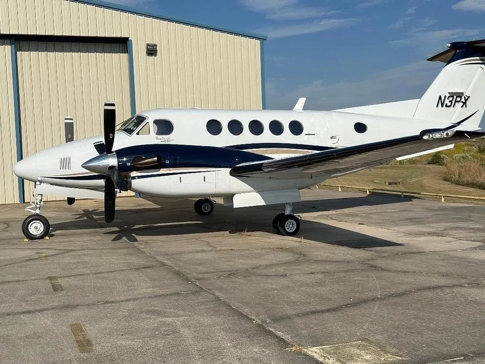 A white and dark blue Beechcraft King Air N3PX is parked on an tarmac next to a hangar.