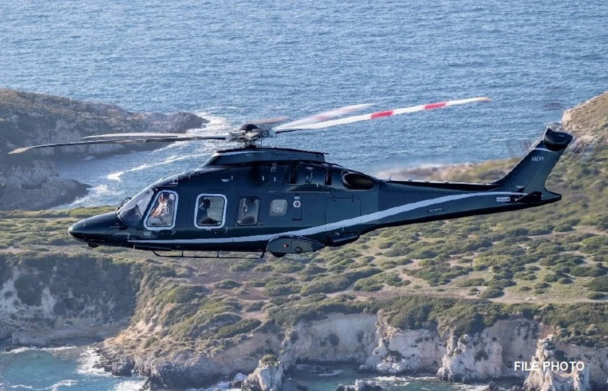 A dark green helicopter flying over the ocean.