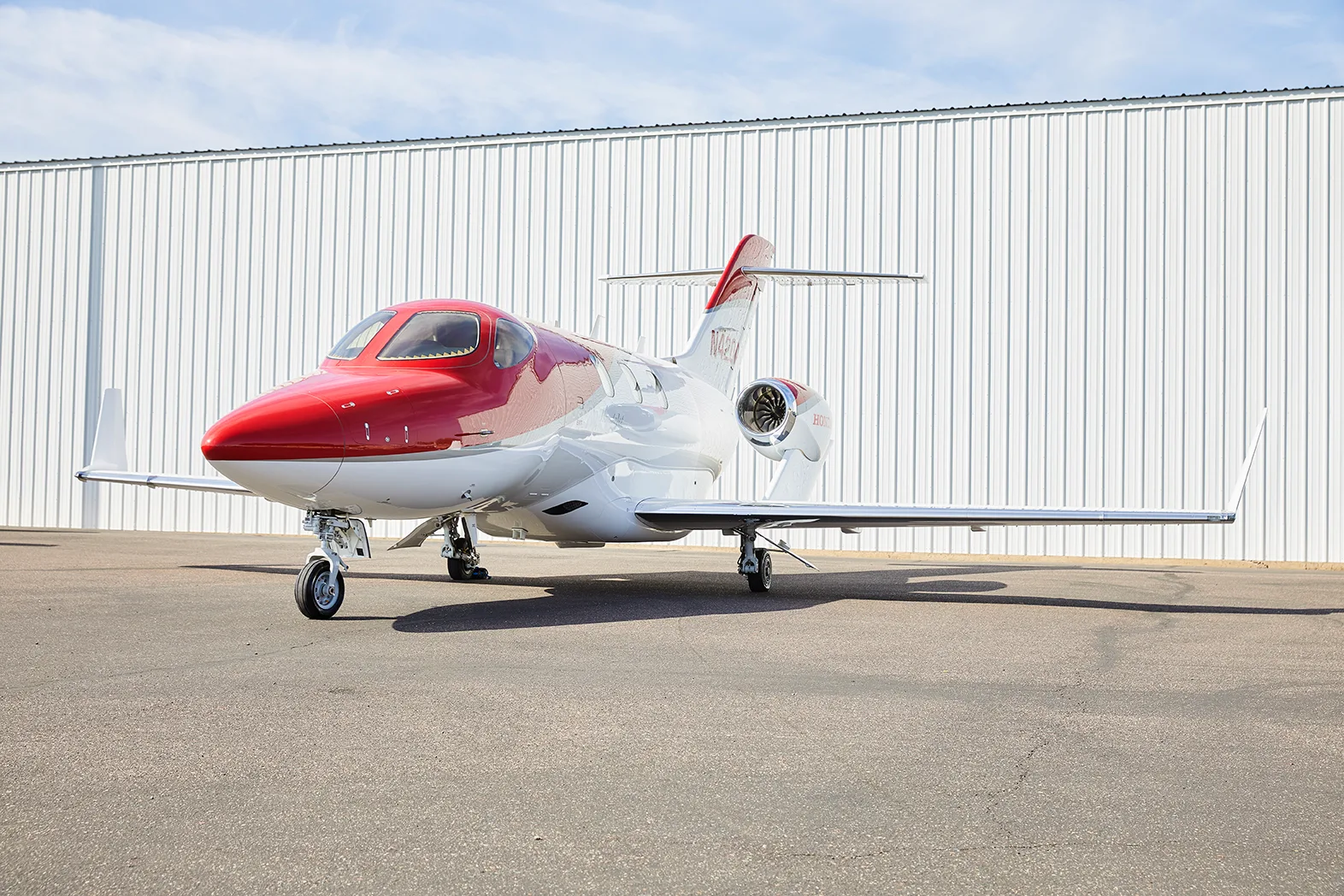 A red and white HondaJet HA-420 aircraft, registration N420AZ, is parked on an asphalt tarmac in front of a white hangar.
