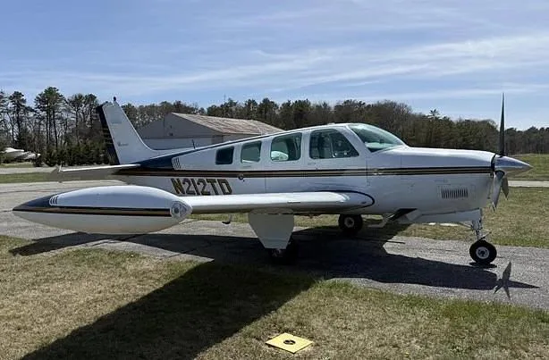 A white Beechcraft Baron N212TD with dark and gold stripes is parked on an airfield ramp.