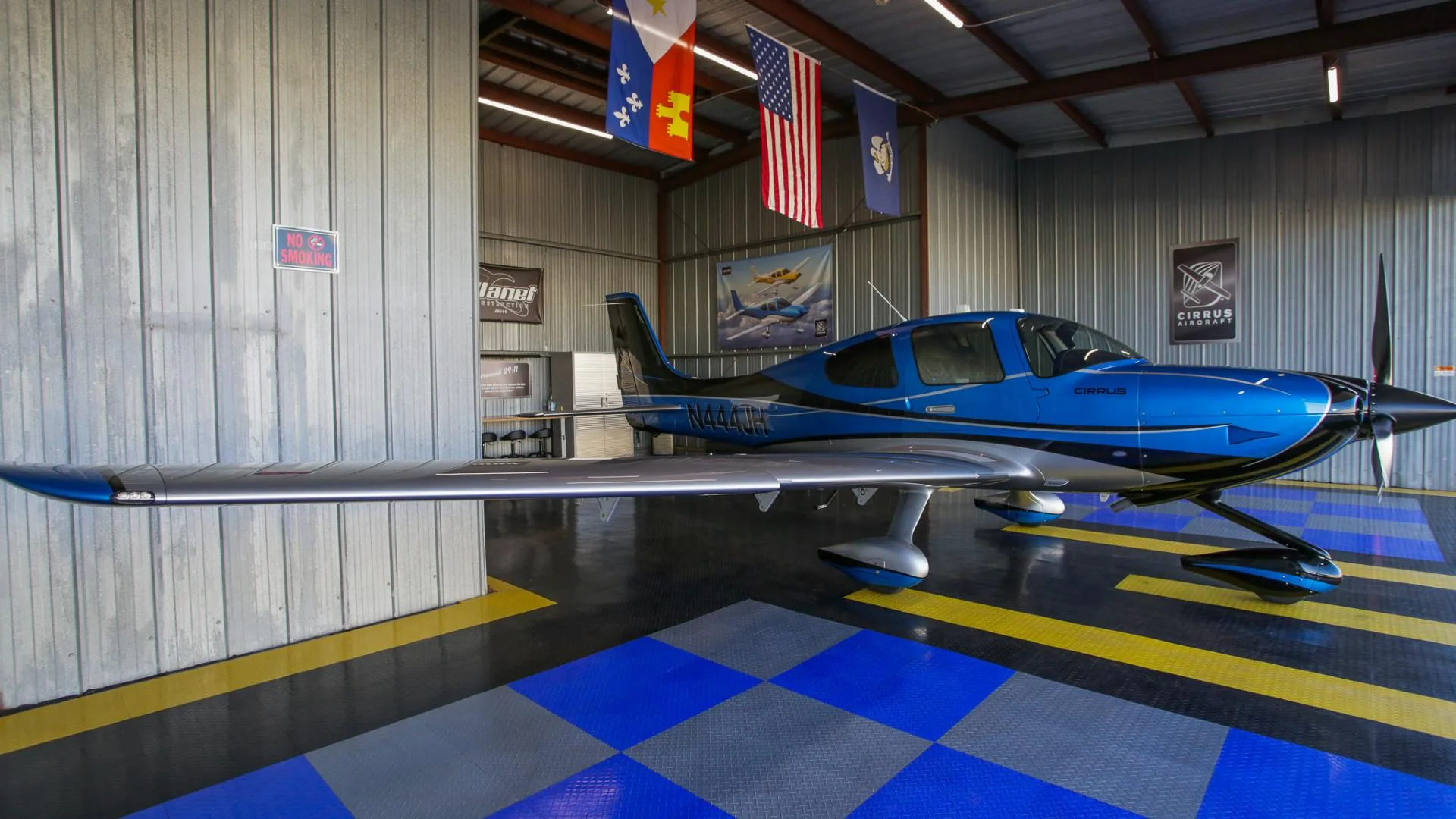 A blue and silver Cirrus SR22 aircraft with registration N444JH parked inside a hangar.