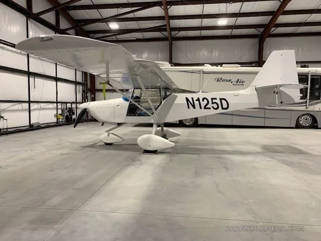 A white Kitfox aircraft with registration N125D, parked inside a hangar next to a large RV.