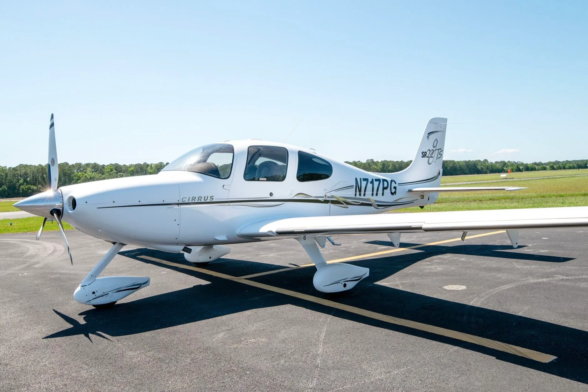 White Cirrus SR22T aircraft N717PG with black and grey stripes parked on an airfield under a clear blue sky.