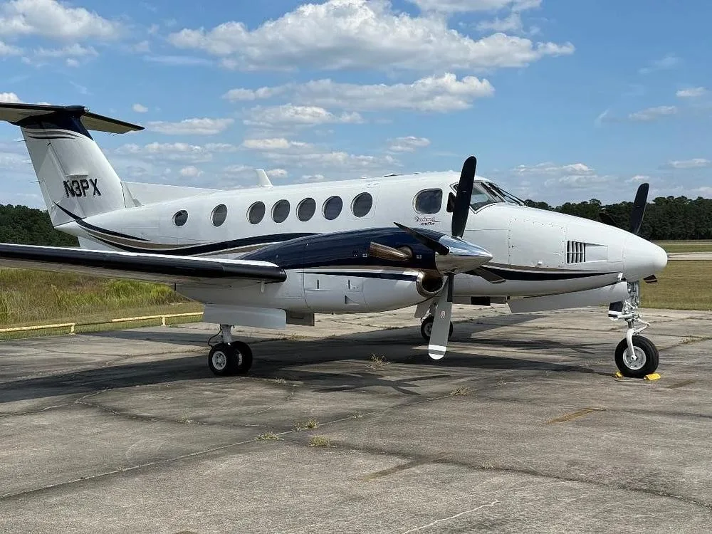 A side view of the white and dark blue Beechcraft King Air N3PX parked on an tarmac.