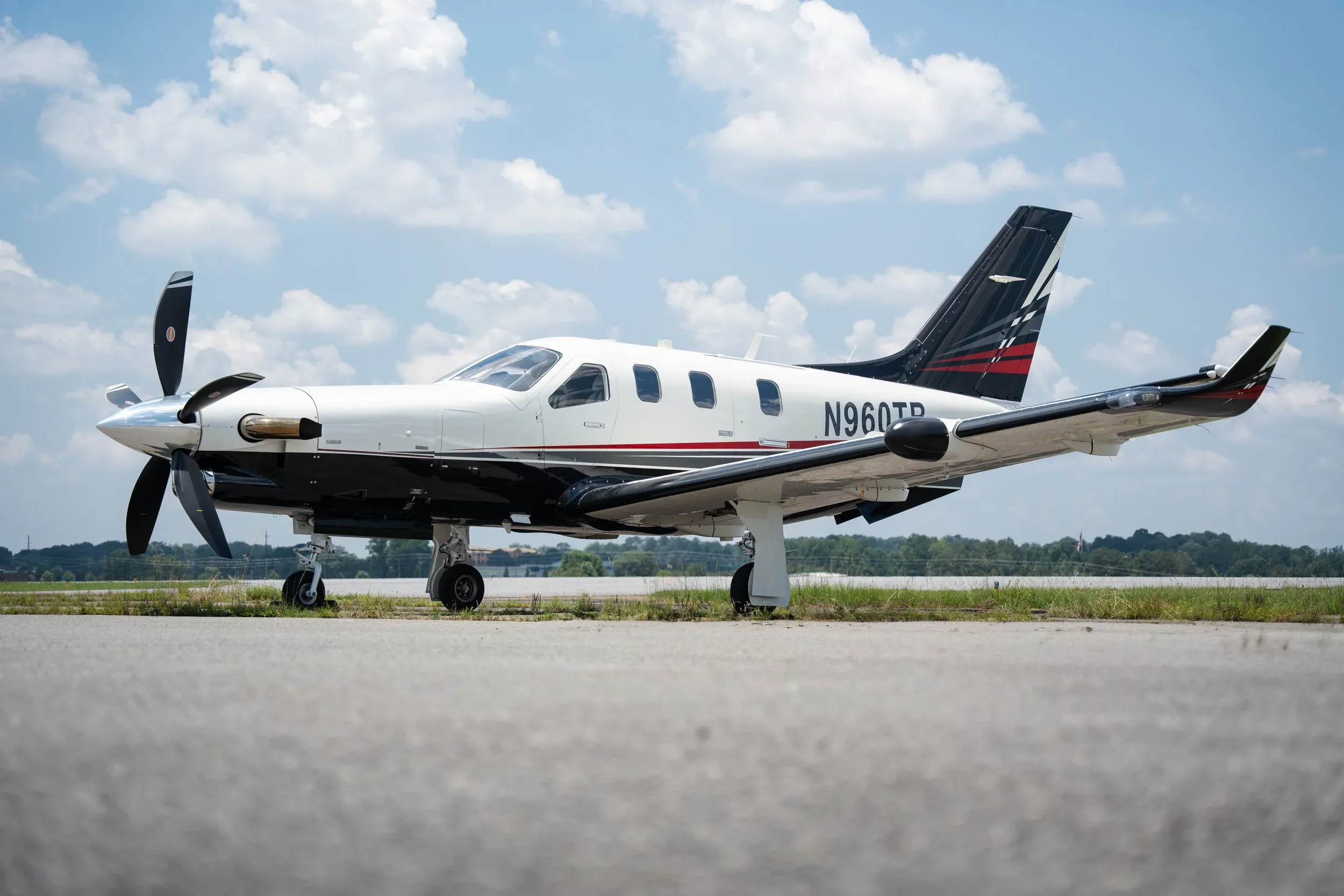 A white and black TBM 960 aircraft with registration N960TB parked on an airport tarmac under a partly cloudy sky.