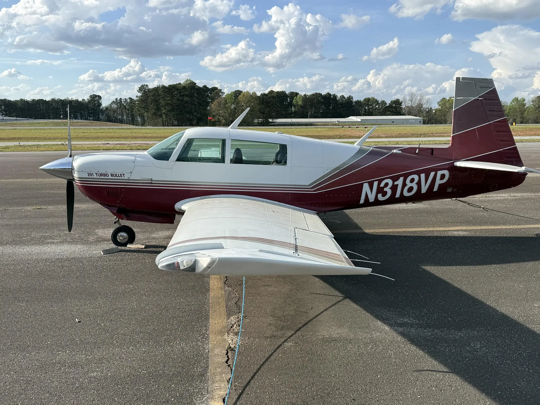 A red and white Mooney 201 Turbo Bullet aircraft, N318VP, parked on an asphalt ramp under a partly cloudy sky.