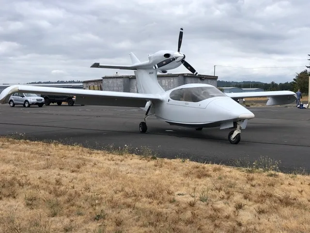 A white Searey amphibian aircraft, N9004T, is parked on an asphalt runway next to a silver car.
