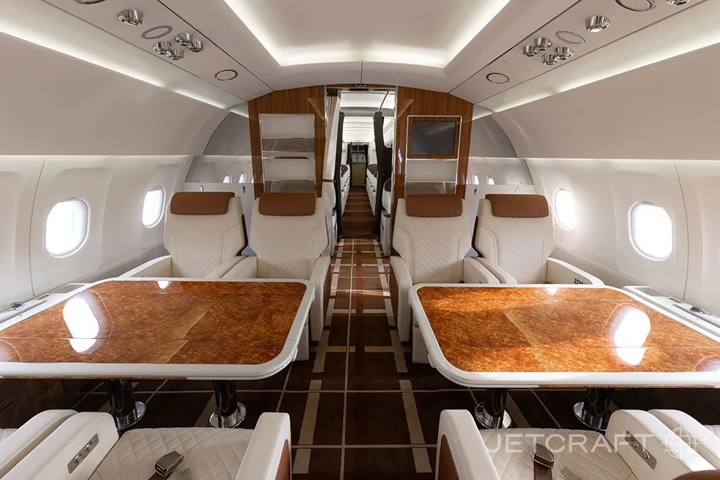 A luxurious aircraft interior with two sets of facing seats and large wooden tables.
