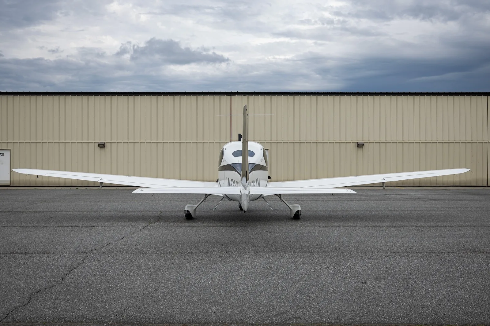 A white and dark blue Cirrus SR22T aircraft with registration N564N viewed from the rear on an asphalt ramp.