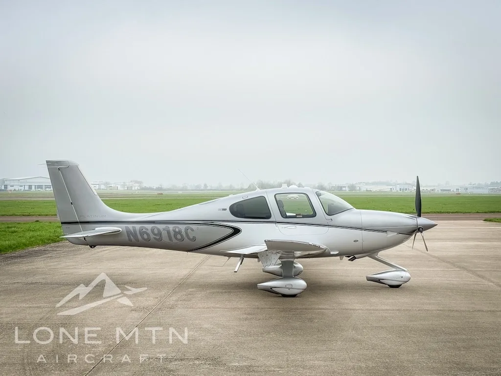 A silver Cirrus SR22 aircraft, registration N6918C, parked on an airfield with a grassy background.