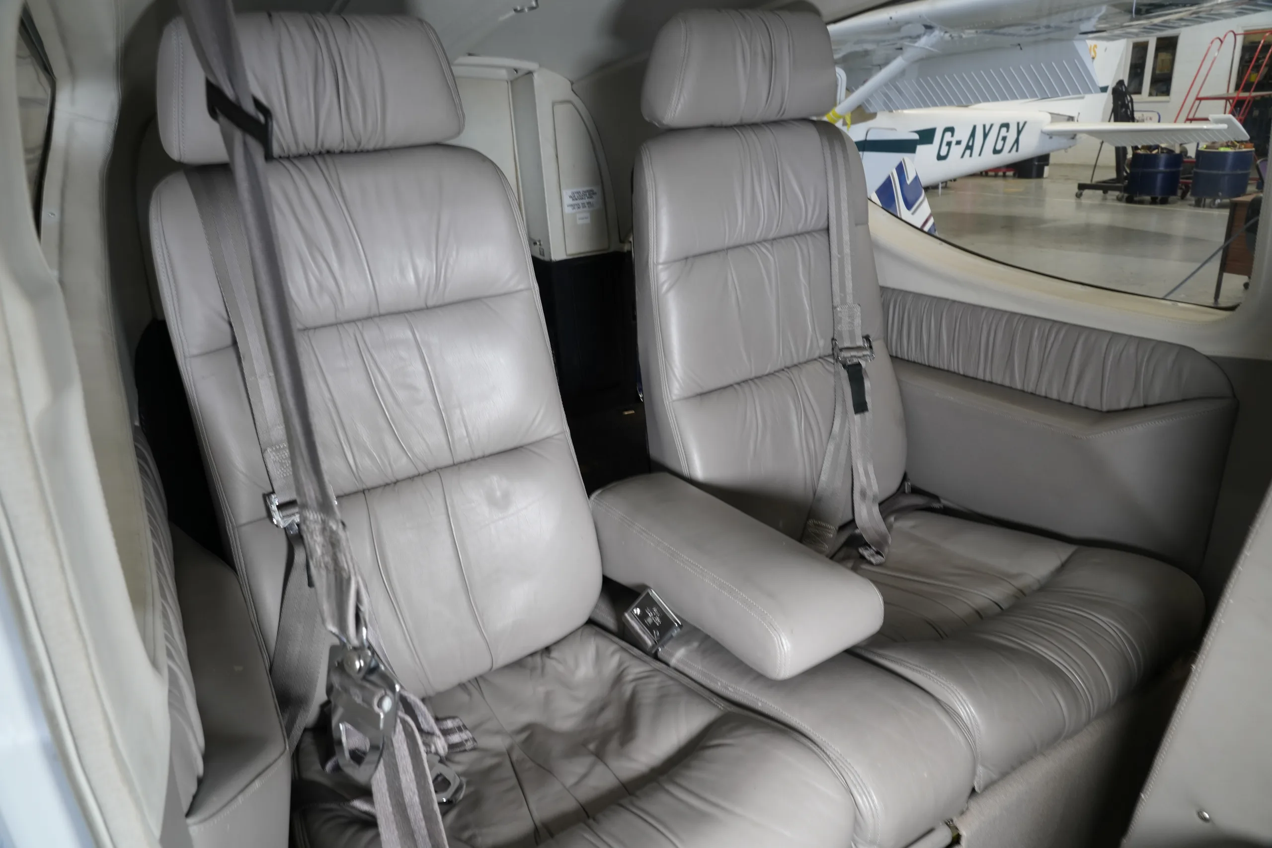Two light grey leather passenger seats in the aircraft cabin, with another aircraft visible outside the window.