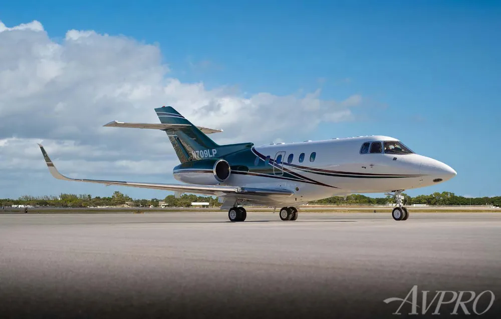 A white and green private jet, N709LP, is parked on an airfield under a blue sky, viewed from the front-right.
