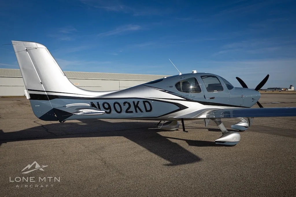 A side view of the Cirrus SR22T aircraft, N902KD, in blue and silver, parked on an airfield.